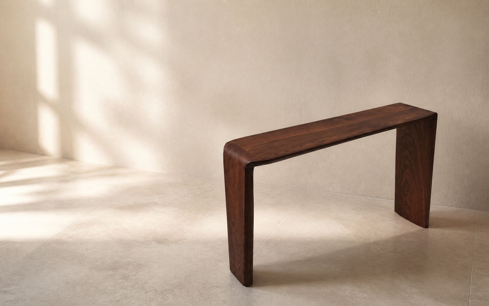 A walnut console with a curved, waterfall top standing against a plaster wall in low afternoon light