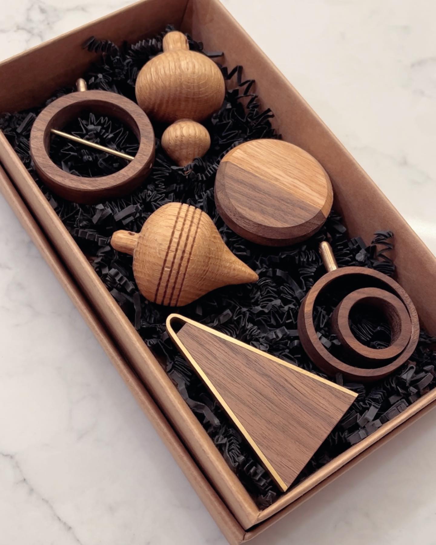 A set of turned and cut ornaments in light and dark wood, packed on black shred inside a kraft box