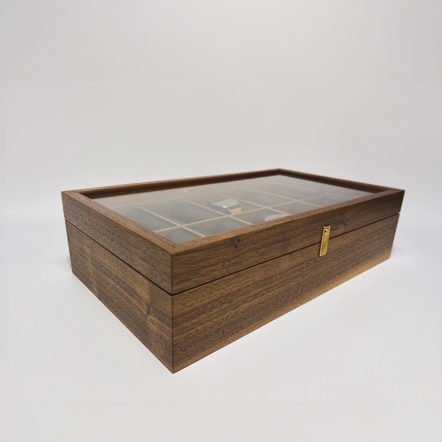 The closed box at an angle, cushions showing through the glass lid and a brass clasp on the front