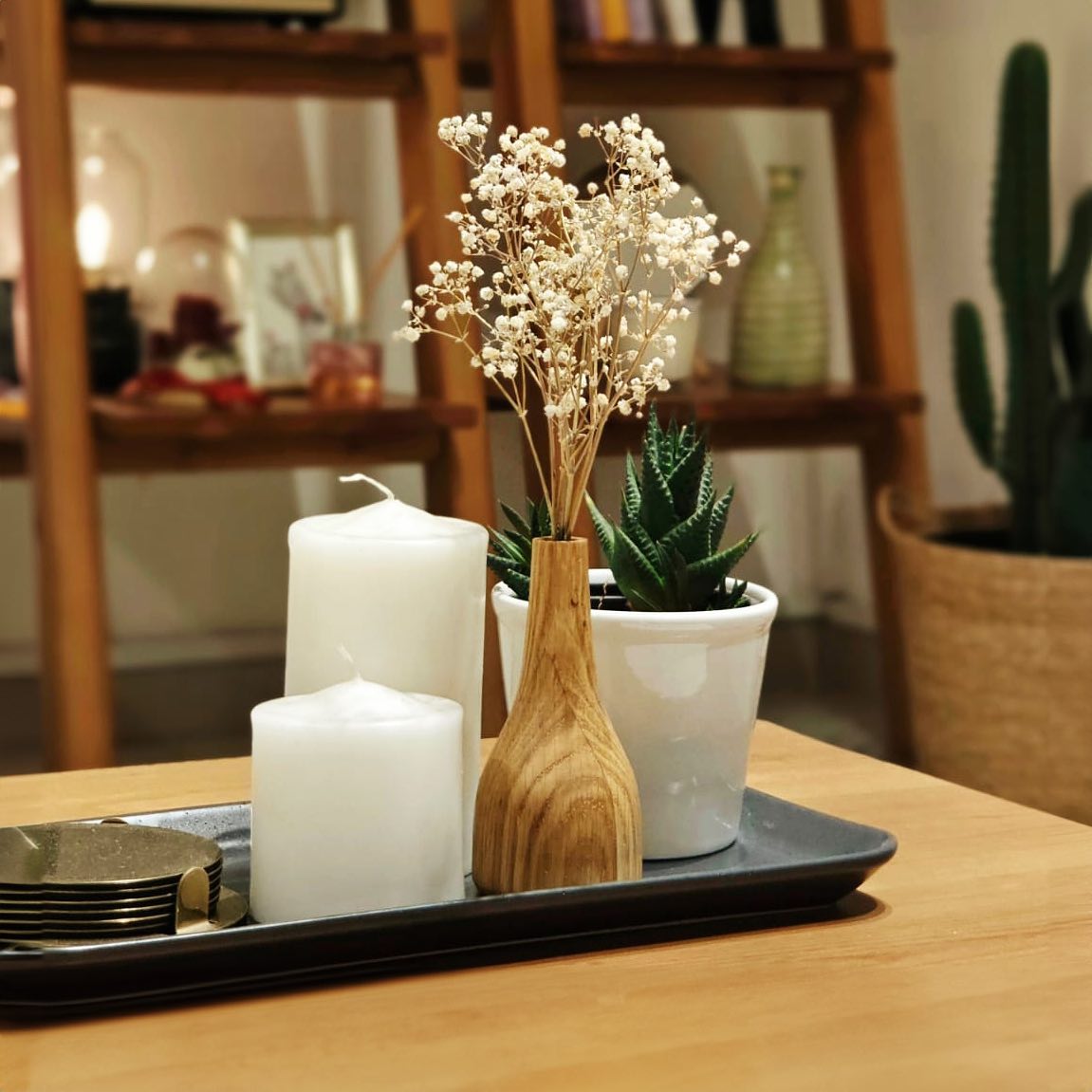 The vase holding dried gypsophila on a dark tray with two pillar candles and a potted succulent