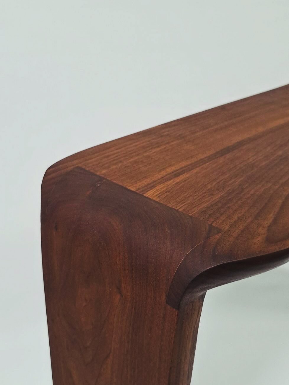 Close view of the corner of a walnut console, where the top curves over into a tapered leg