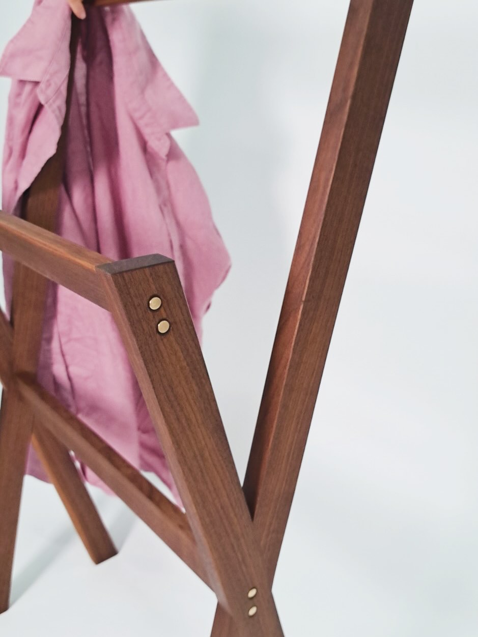 A pink linen shirt draped over the frame, brass pins catching the light at the joints