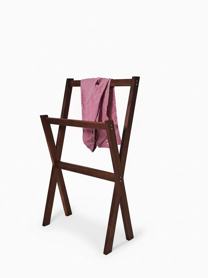 The valet stand carrying a folded pink shirt over its upper rail