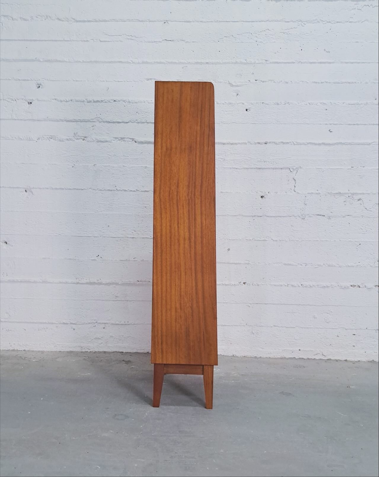 The bookcase seen edge-on, showing its shallow depth and softly rounded top corner