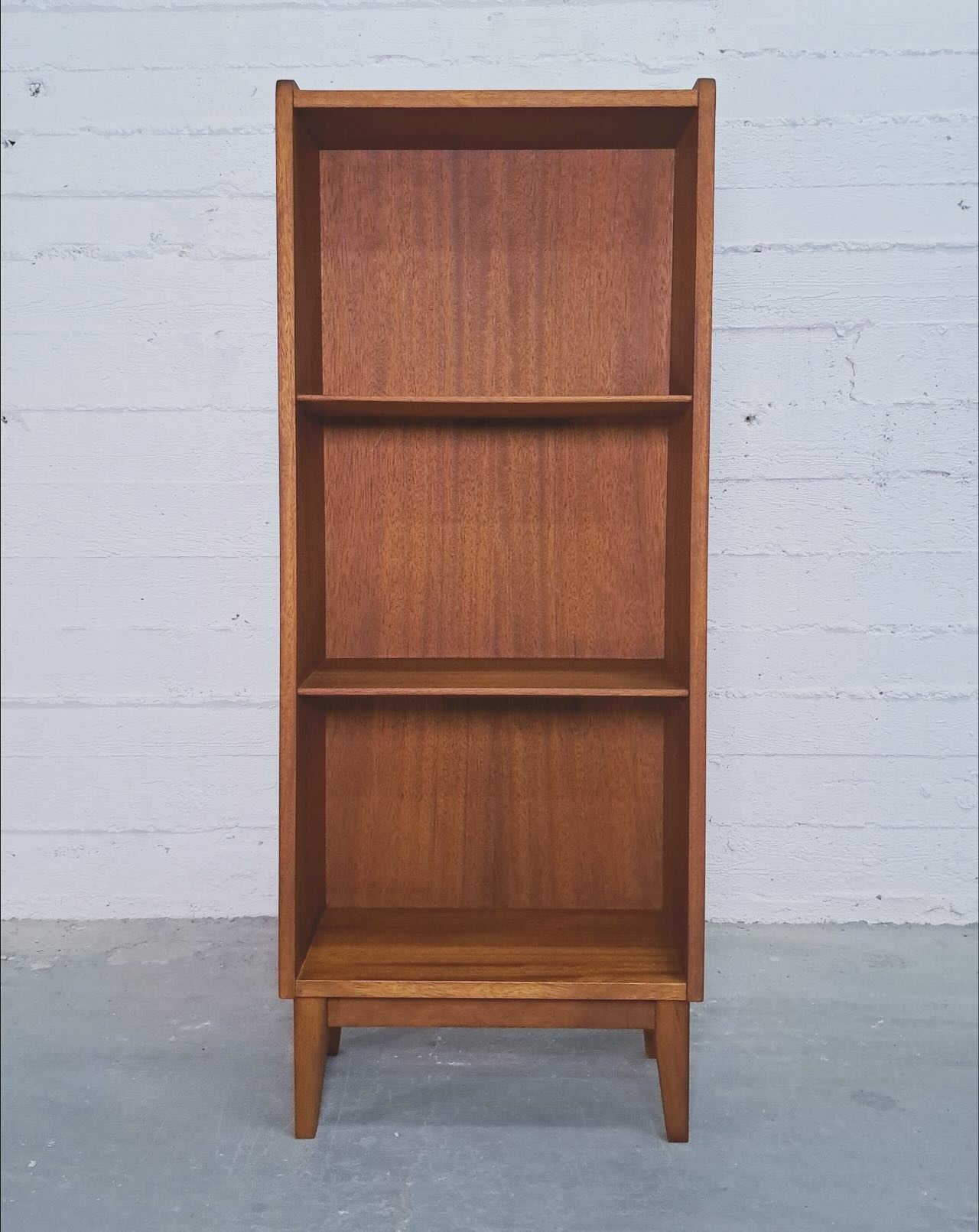 The bookcase straight on, empty shelves above a tapered leg base that lifts it off the floor