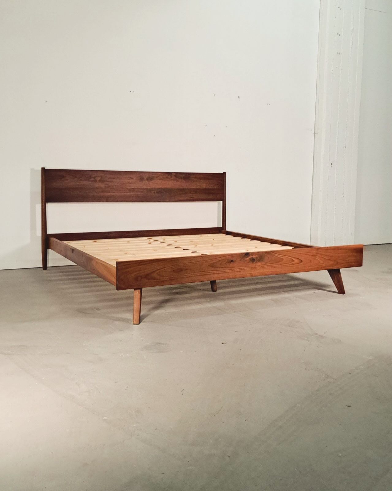 The bed frame at an angle against a white wall, pale slats laid across the empty frame